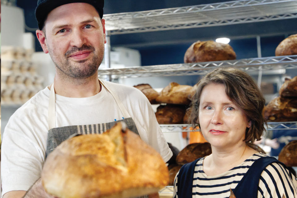 a man holding a loaf of bread next to a woman.