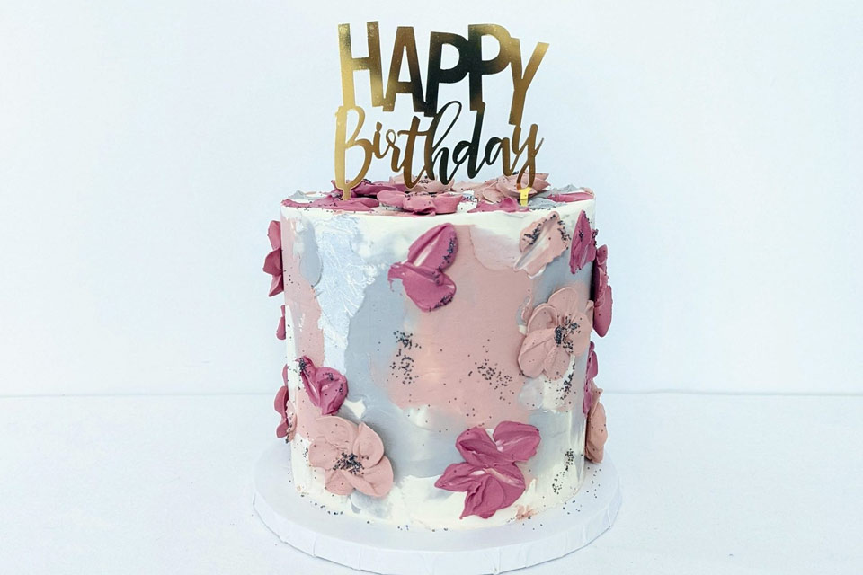 a birthday cake decorated with pink flowers and a happy birthday sign.