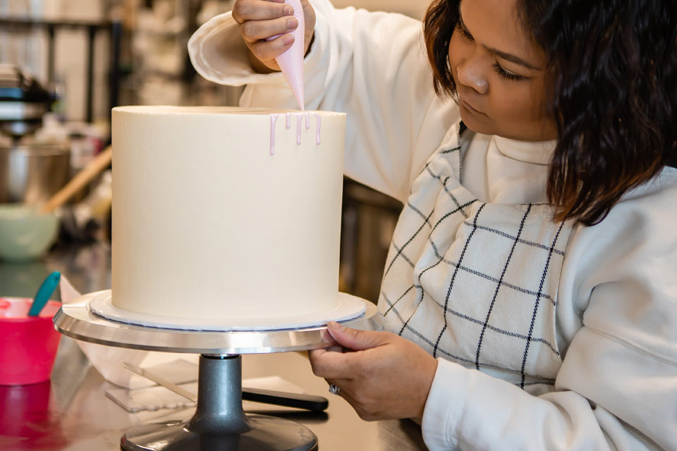 a woman decorating a white cake with pink icing.