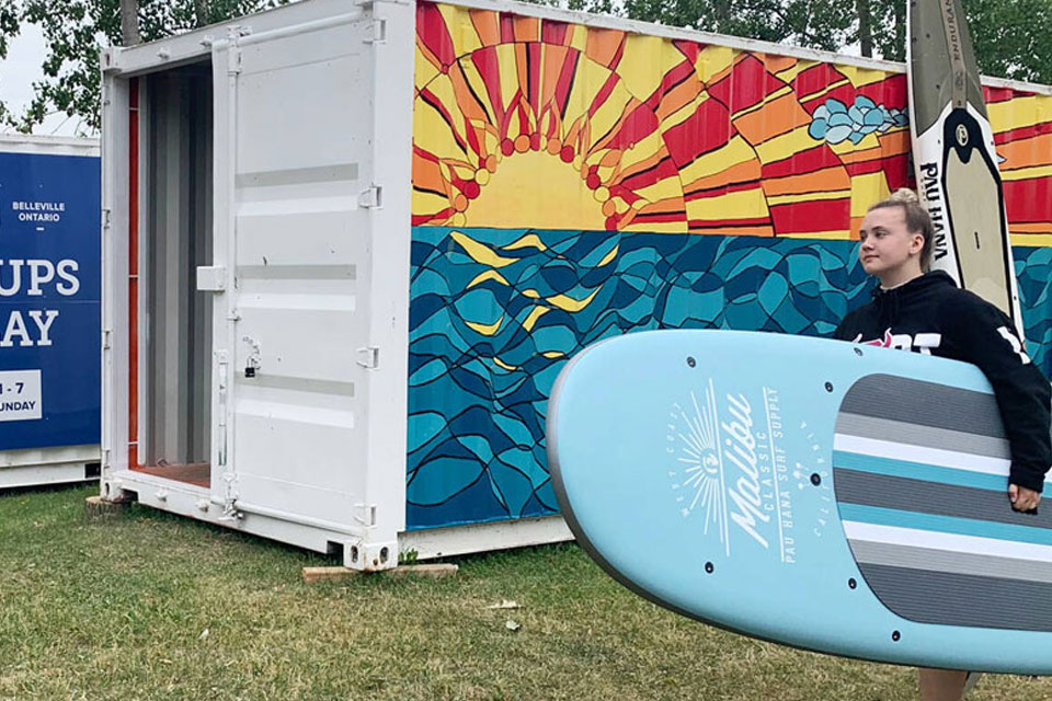 a man holding a surfboard next to a portable toilet.