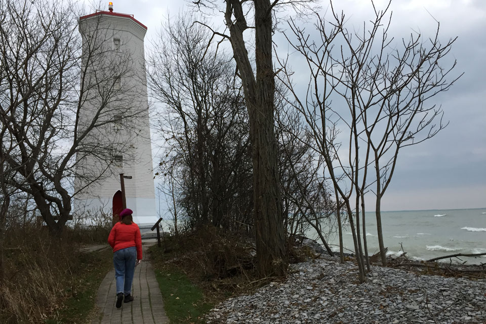 a woman in a red jacket is walking towards a lighthouse.