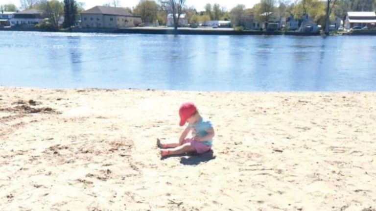 a little girl sitting on top of a sandy beach.