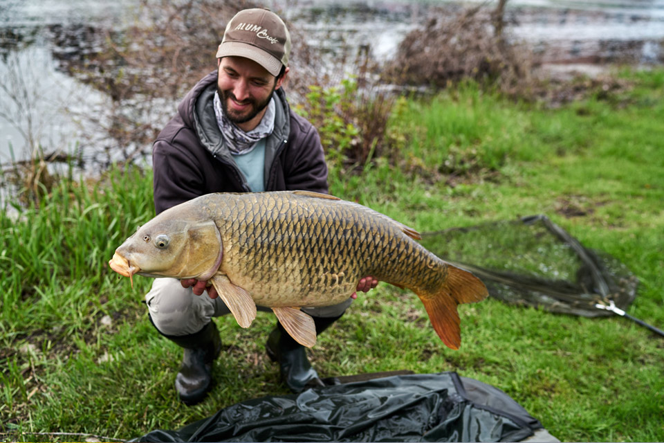a man crouching down and holding a large carp.