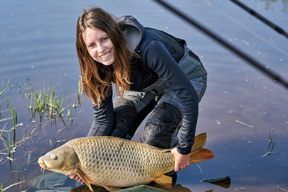 a woman is holding a large carp in the water.