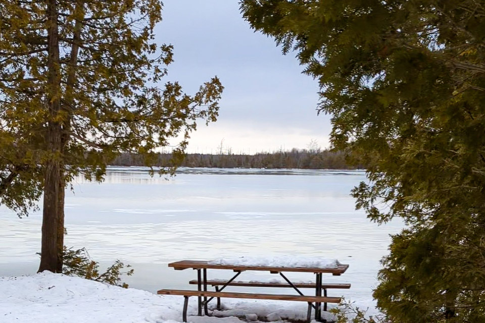 a picnic table in the snow near a lake.