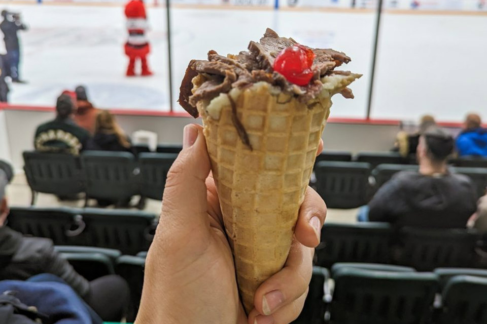 a person holding an ice cream cone in front of a hockey game.
