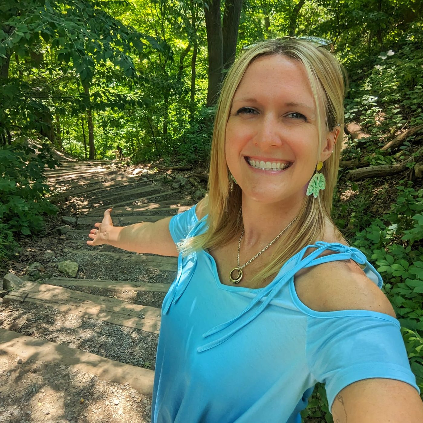 A woman in a blue shirt standing on steps in the woods.