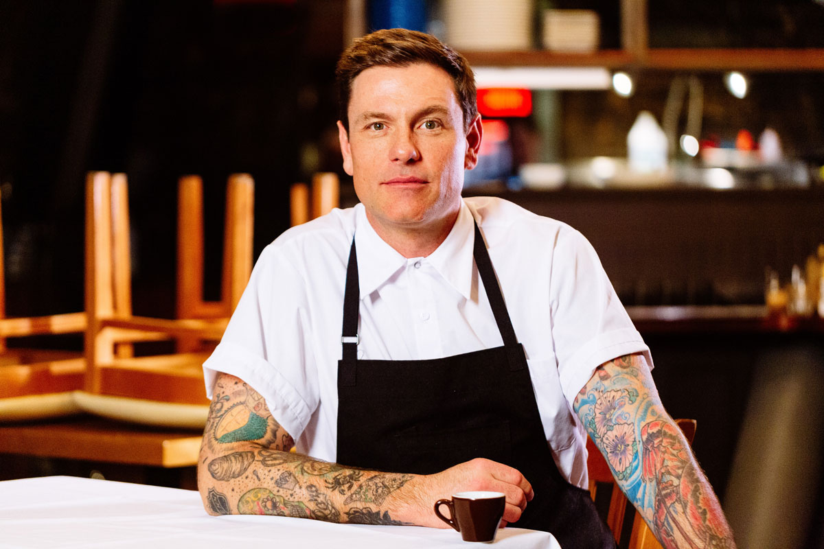 man with tattoos in a white button up shirt with an apron