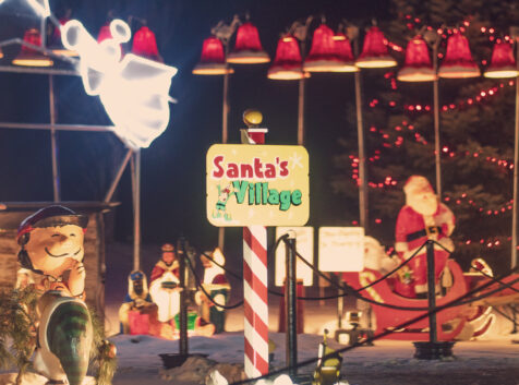 holiday light display with a sign that says Santa's Village with santa in a sleigh and bells all around