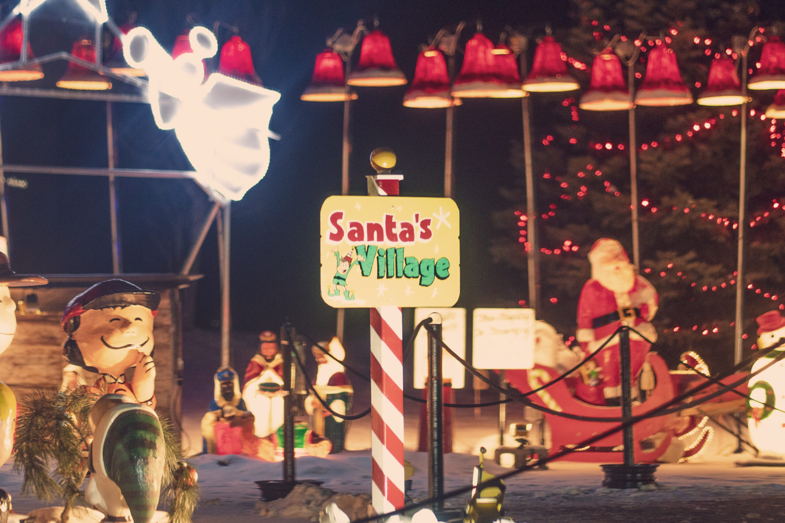 holiday light display with a sign that says Santa's Village with santa in a sleigh and bells all around