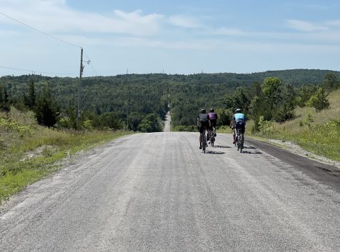 three cyclists cresting over a hill on a gravel backroad