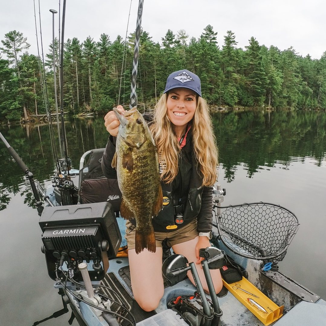 white woman with blond hair on a fishing kayak holding up a fish
