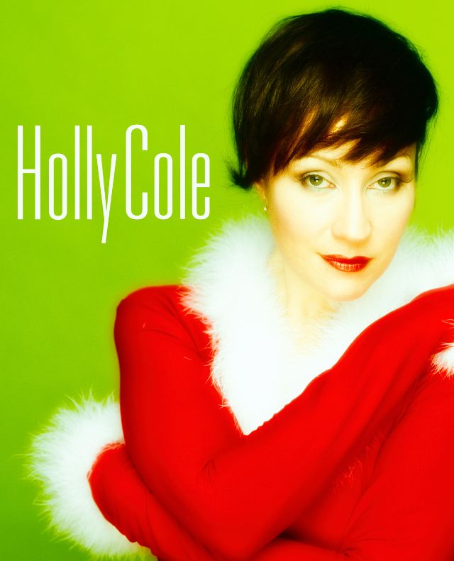 Image of singer Holly Cole wearing red and white "christmas" themed sweater with a green backdrop.