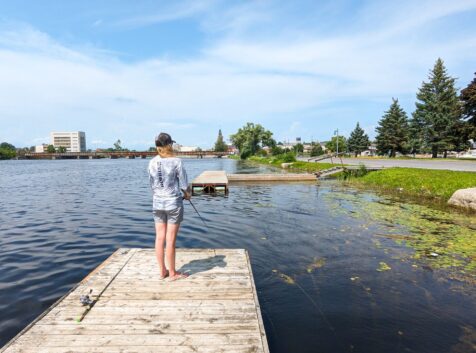 woman standing on a dock fishing by the shore