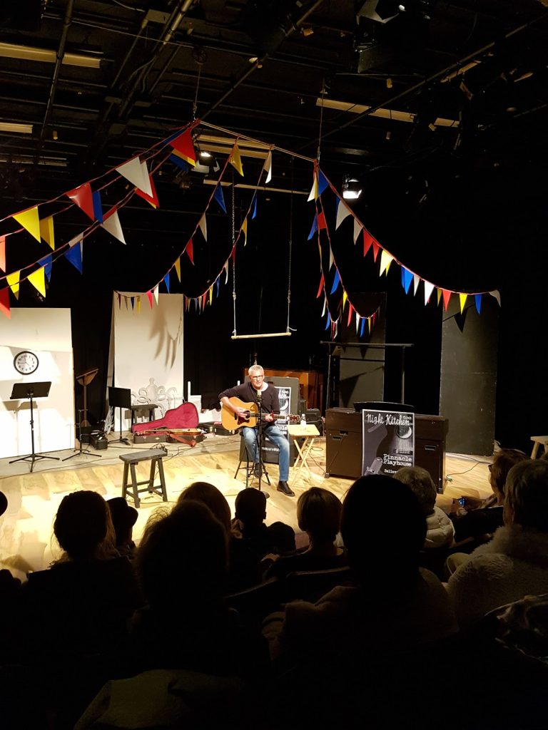 Photo of performer on stage with acoustic guitar at the Pinnacle Playhouse.