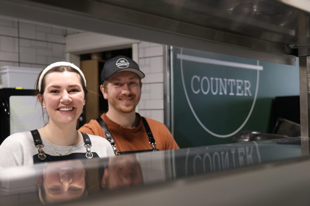 Owners of The Counter, Kylie and Braden, standing behind the service counter in their restaurant