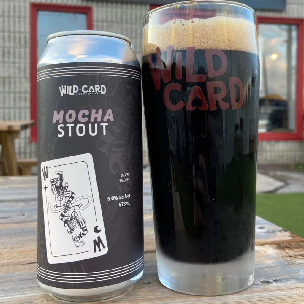 a pint glass full of dark stout beer with a can beside it
