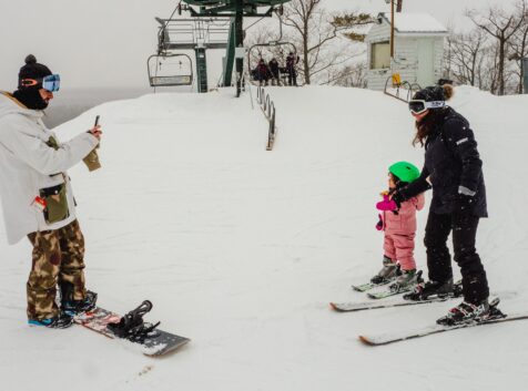 a man taking a photo of a woman and child on a ski hill