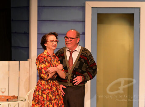 a man and woman in old-fashioned clothing on stage at a community theatre