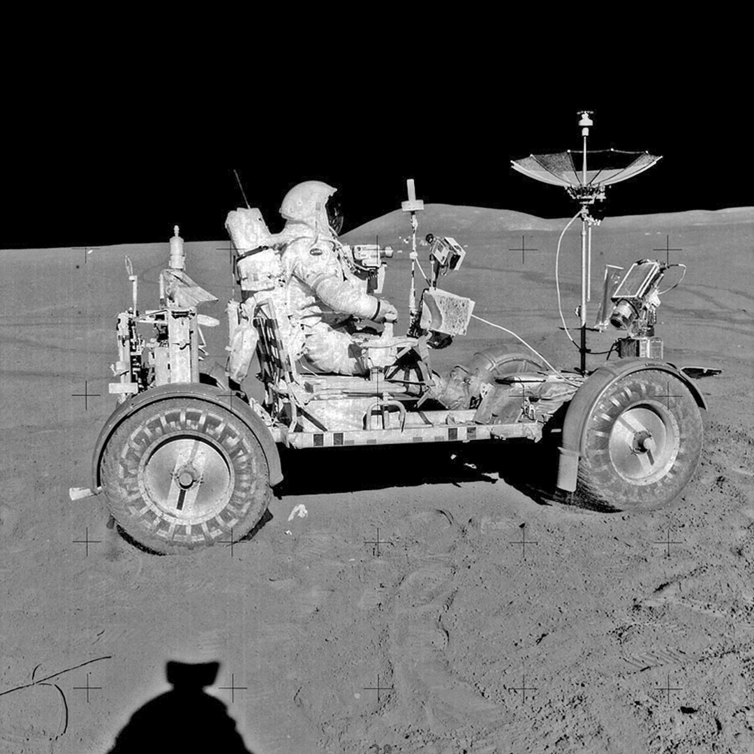 black and white photo of an astronaut riding a rover.