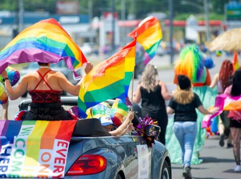 A Pride parade making its way down the street with participants waving rainbow flags