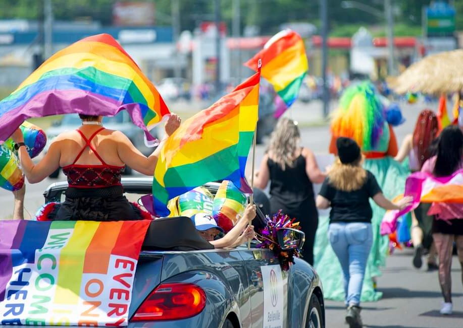 A Pride parade making its way down the street with participants waving rainbow flags