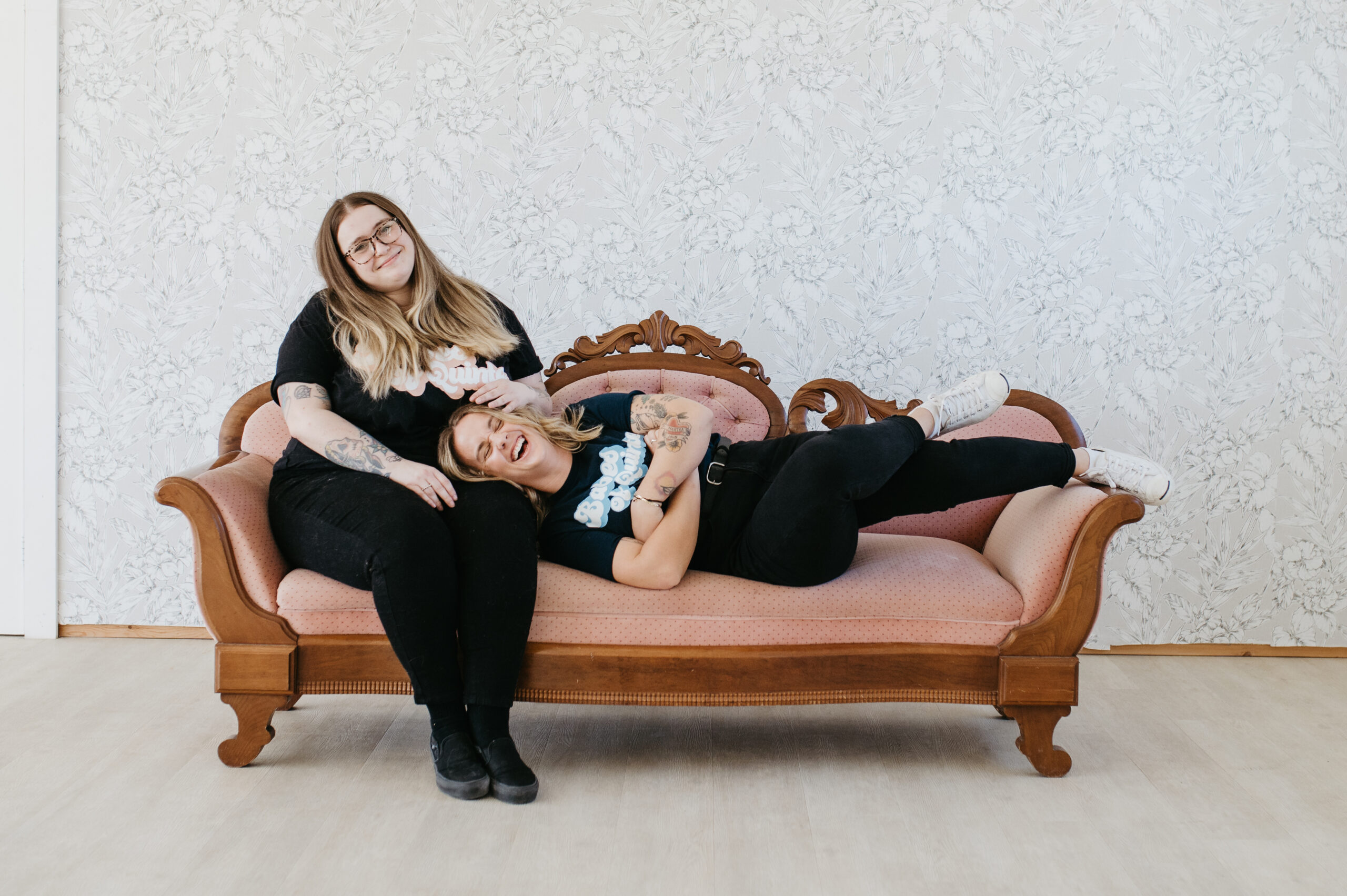 two women (light skin, blonde hair) posing on an antique couch