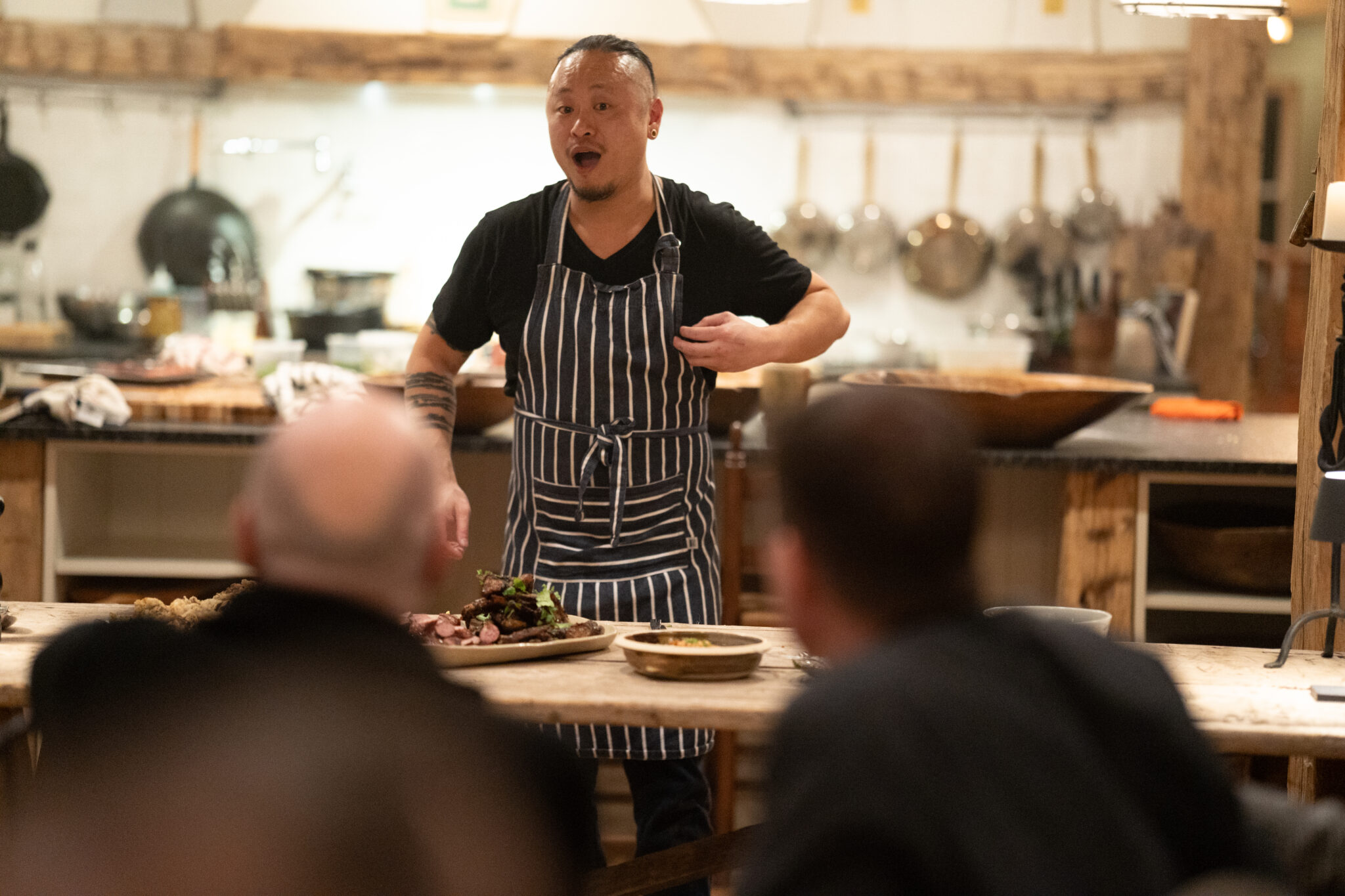 a chef talking to a group of people dining in a farmhouse kitchen at a farm to table supper experience