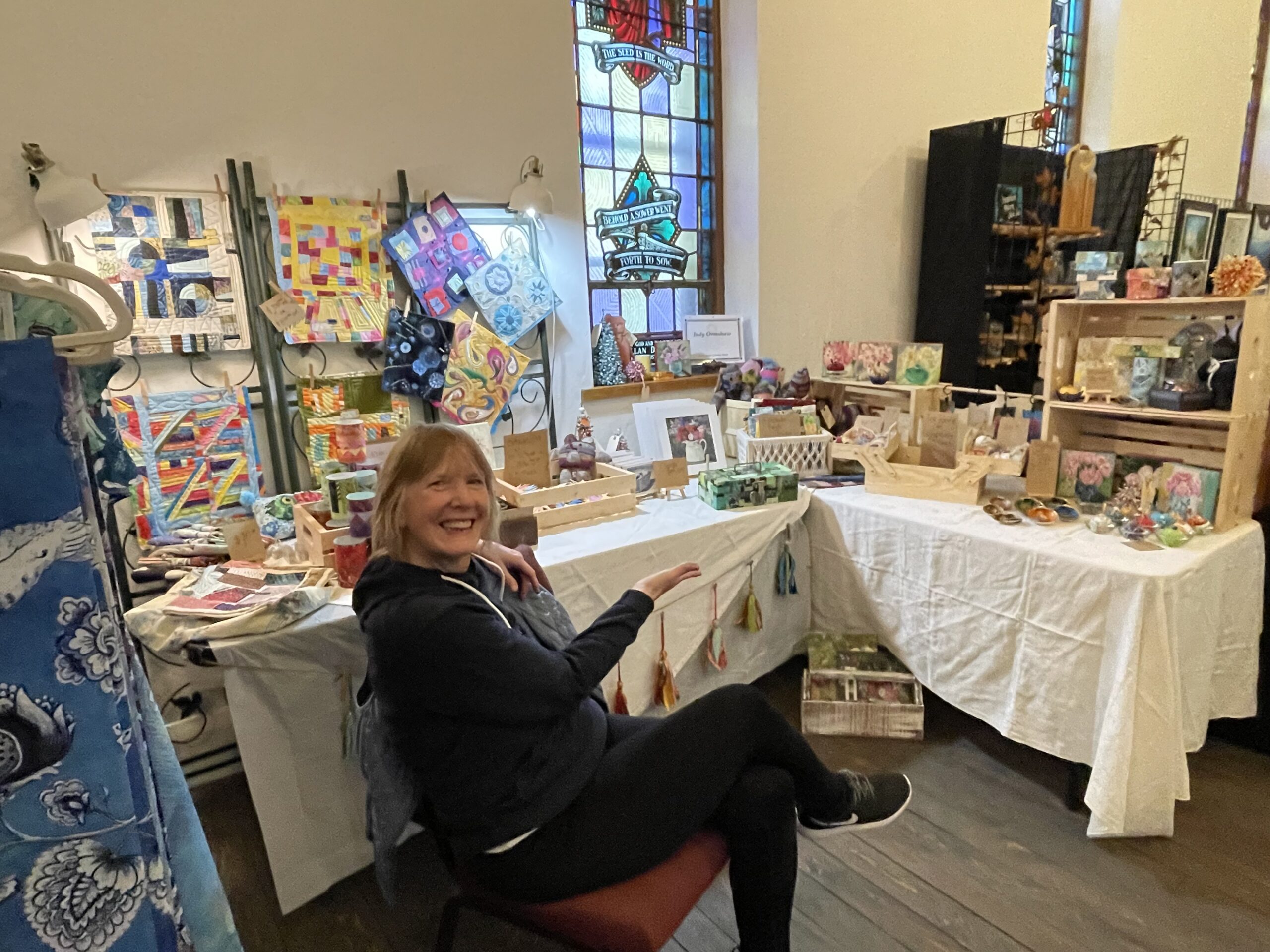 an artist sitting at a booth at a vendor show surrounded by paintings