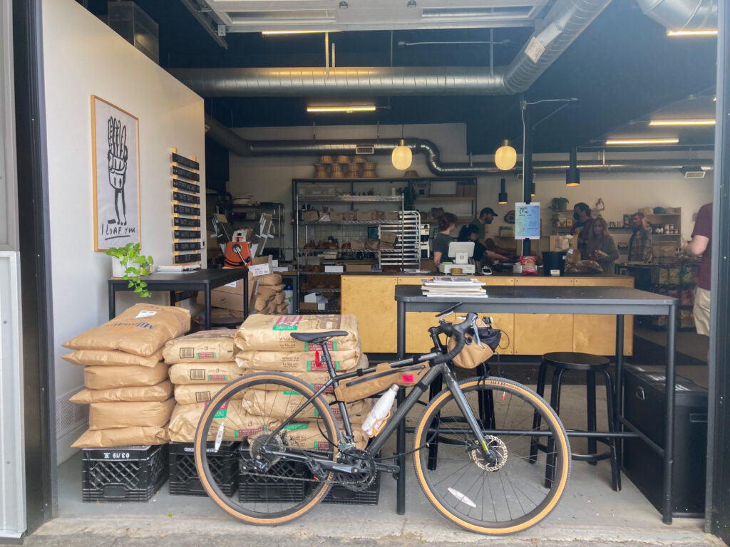 a bicycle leaning against bar seating of a modern bakery, where the garage door is open to show the whole space from the outside