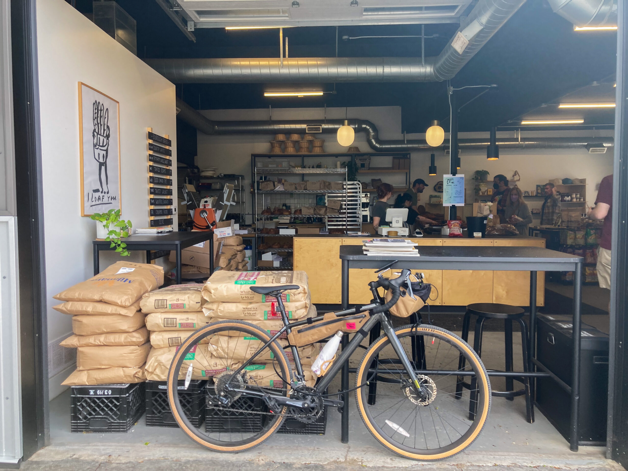 a bicycle leaning against bar seating of a modern bakery, where the garage door is open to show the whole space from the outside