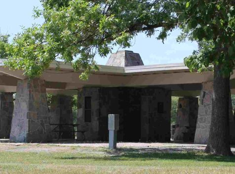 A photo of an open-air structure with collumns in a park with trees.