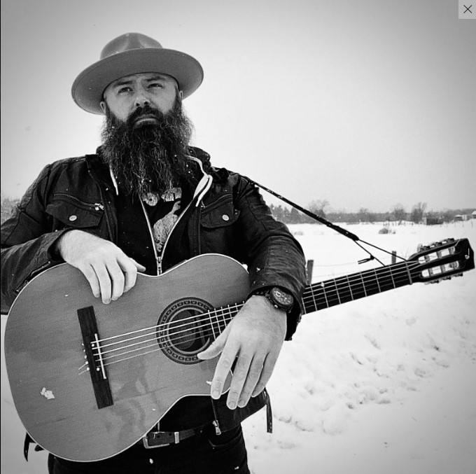 Photo of perfromer Wade Barras holding an acoustic guitar.