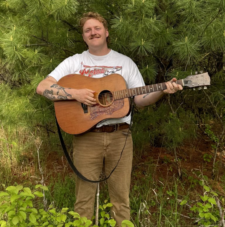 Photo of performer holding an acoustic guitar.