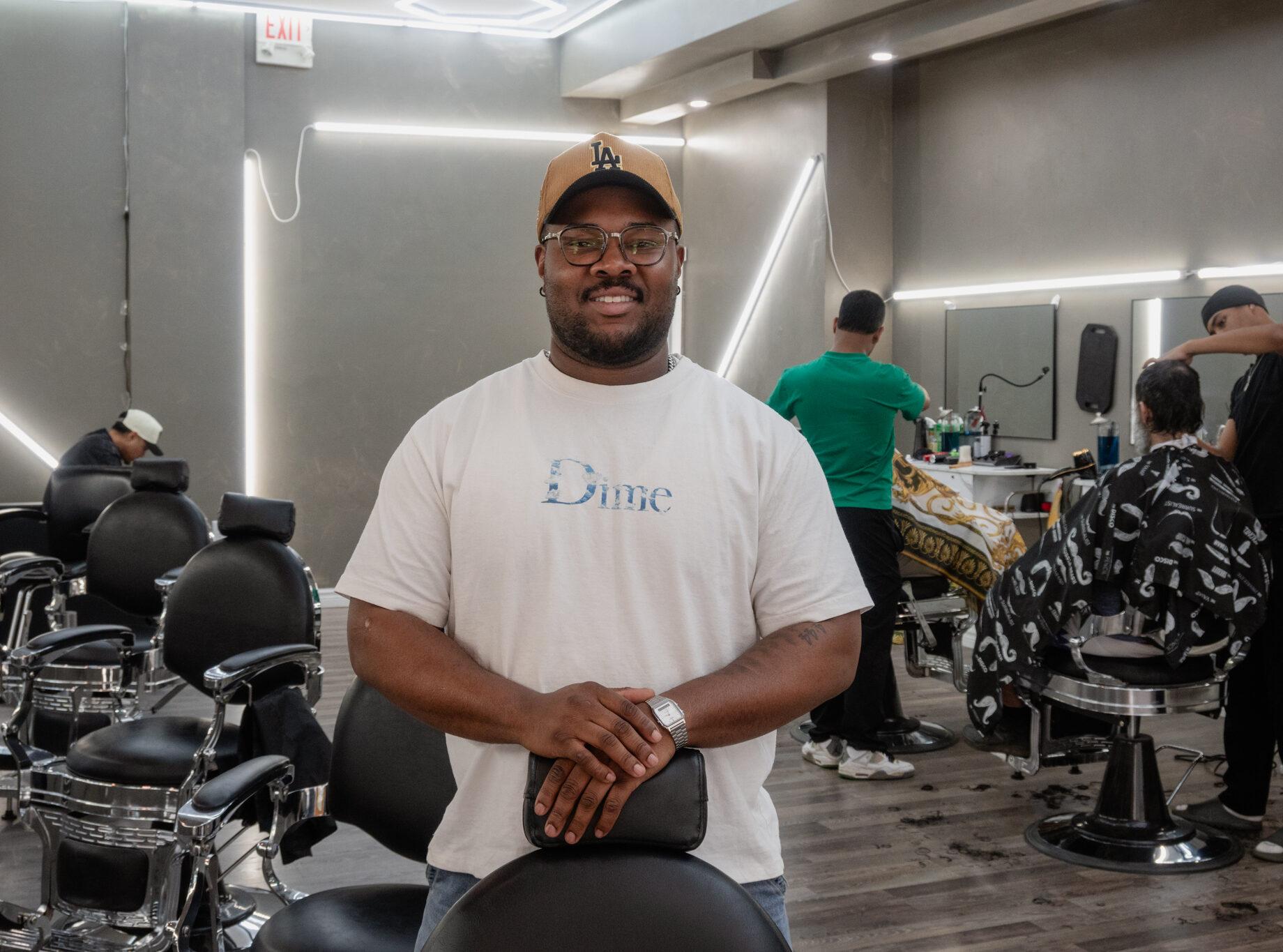 Kam, owner of revive studios, poses for a photo leaning on one of the barber chairs with two employees working in the background
