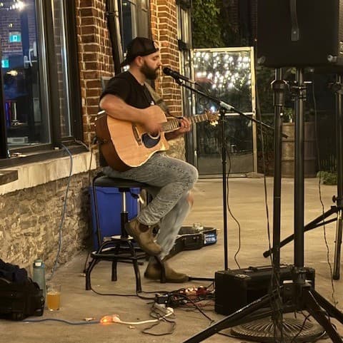 Man plays guitar and sings into mic facing the side